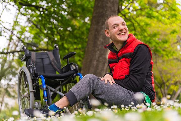 disabled man sitting on ground in park in front of wheel chair